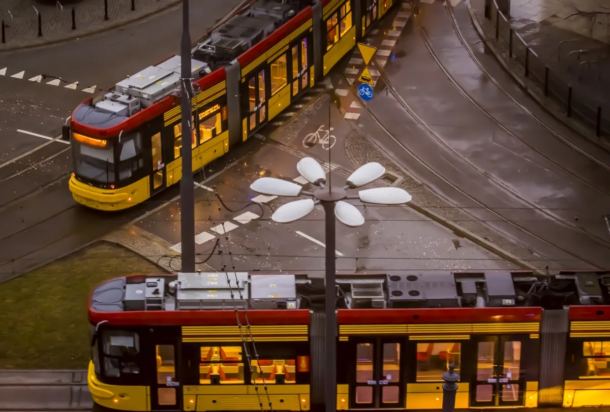 Two yellow trams crossing at a wet intersection